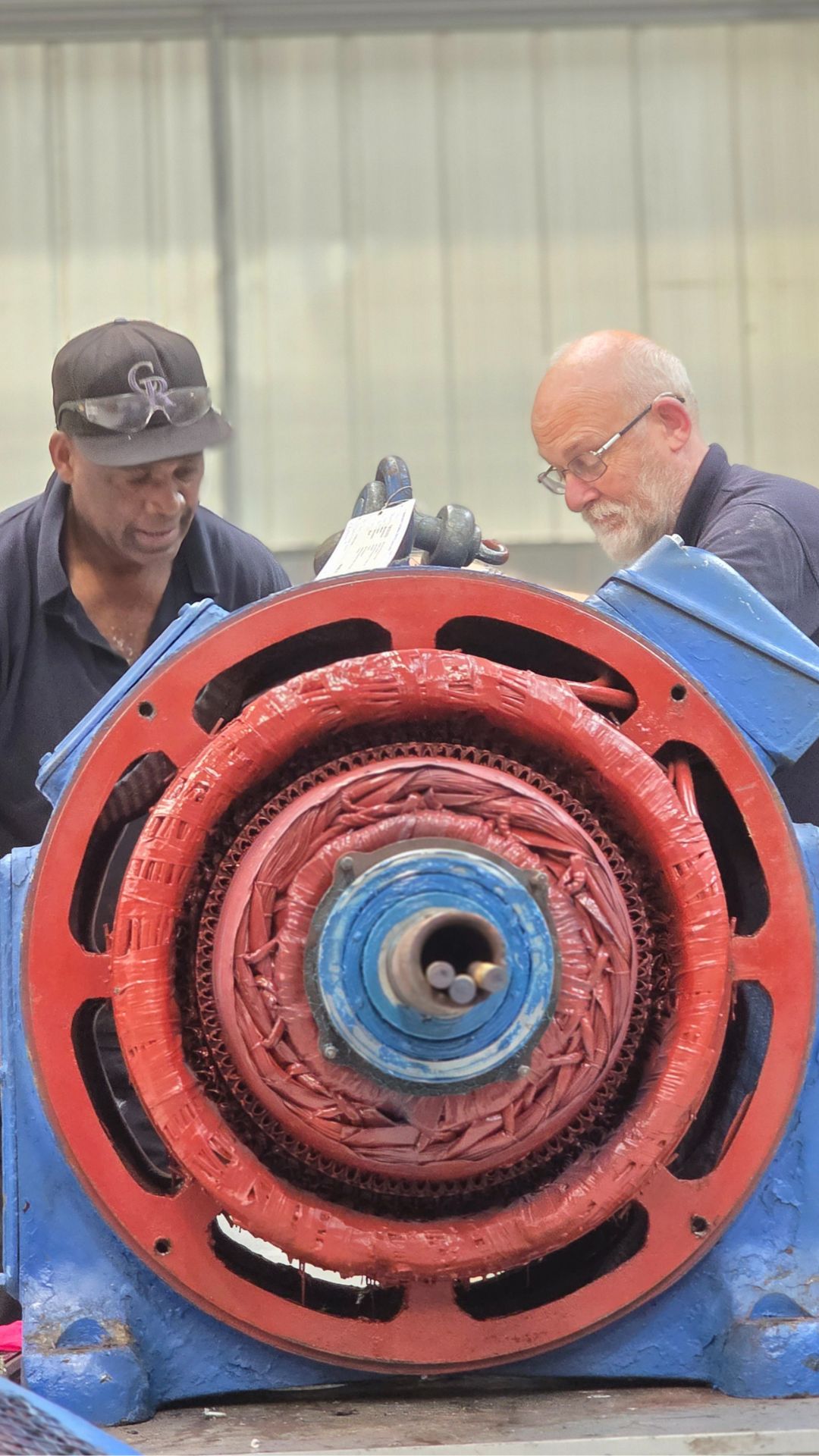 Two technicians performing electric motor rewinds on a large industrial motor featuring blue and red components and visible internal coils in the Neutronic Technologies workshop.