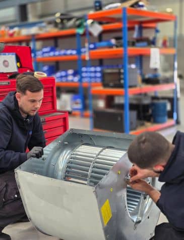 Engineers carrying out fan repair at Neutronic Technologies workshop, inspecting and adjusting a industrial fan housing with an impeller on a workbench.