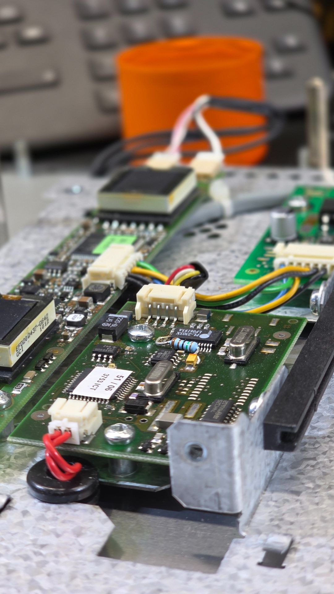 Close-up of an HMI (Human-Machine Interface) circuit board during repairs, featuring electronic components like resistors, capacitors, and multicolored wires, with blurred industrial tools in the background.