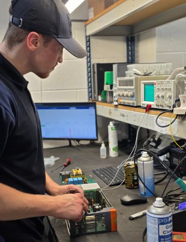 An engineer is performing servo drive repairs at an electronics workbench using testing equipment and diagnostic tools at Neutronic Technologies.